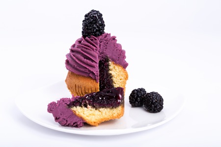 mulberry sweet cupcake cut with a berry on the top on a white background.の写真素材