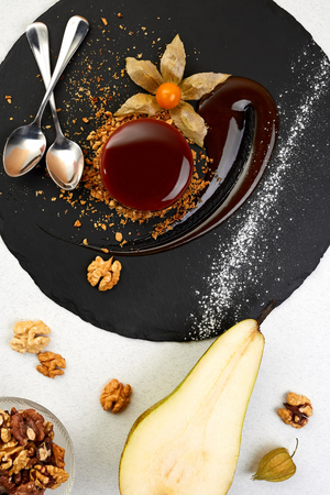 Delicious Chocolate glazed circle cake on black shale. Chocolate dessert with pear and Walnut. Restaurant Stylized composition on white backgroundの写真素材