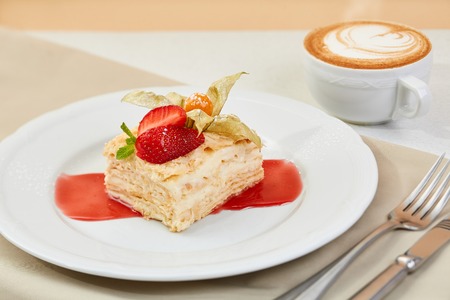napoleon cake with strawberry, Physalis and jam on white plate. mille-feuille dessert with coffee and cutlery on the tableの写真素材