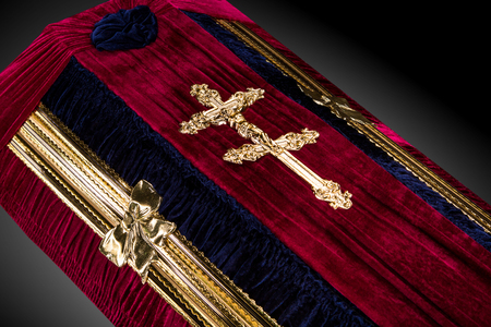 closed red velvet coffin covered with cloth isolated on gray background. coffin close-up with gold Church cross.の写真素材