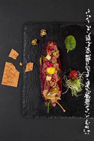 fresh beef tartar with salt and herbs and Crispbread, studio shot. Meat tartar on black shale. On white backgroundの写真素材