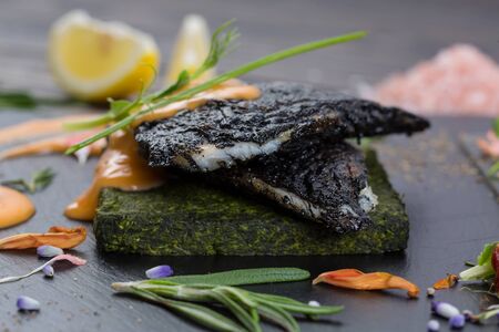 Groupers grilled fillet on a spinach bed. Fish on the black slate, shale board. Lemon pieces, sauce and rosemaryの写真素材