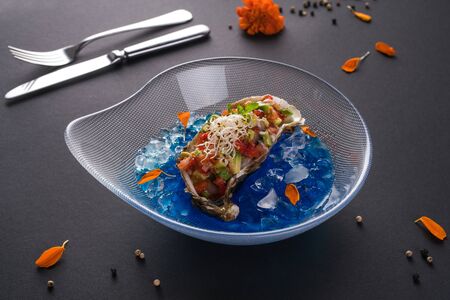 oyster tartare. Fish delicacy on blue ice. Beautiful serving of seafood on a black background