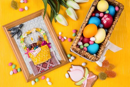 Easter colorful background. Painted eggs in a basket, sweets and flowers on a colored orange...