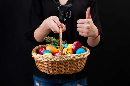 Woman holding basket with colorful easter eggs and showing thumbs up. Hands holding easter basket on black background.の写真素材