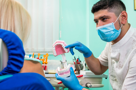 Dentist showing a model of teeth and jaw to his patient in stomatology clinicの写真素材