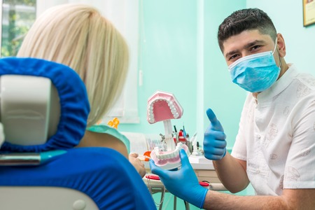 Dentist showing a model of teeth and jaw to his patient in stomatology clinic. The dentist looking...