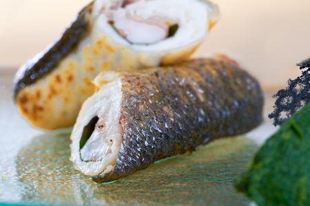 Fried fish roll on glass plate. Fresh seafood, closeup view on blurred background.