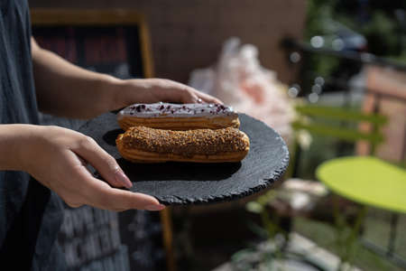 Raspberry and caramel eclair on round black rock stand in hands. Sweets to order concept. Two...