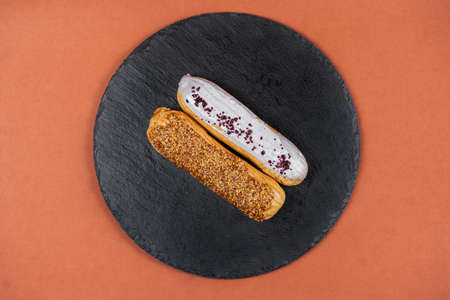 Raspberry and caramel eclair on round black rock stand on brown background. Eclairs with white glaze...