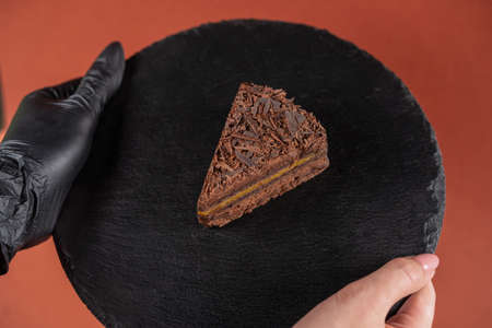 Chocolate cake on round black rock stand in hands. Confectionery concept. Cake with chocolate chip...