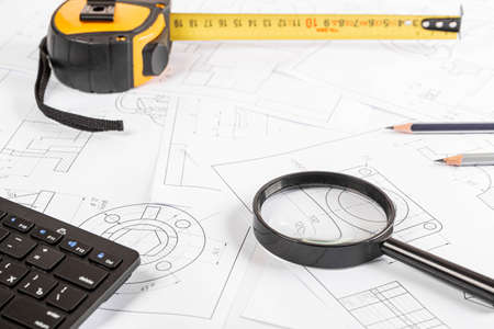 Magnifier, measuring tape, keyboard and pencils on the background of drawingsの写真素材