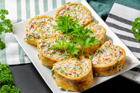 Sliced cheese omelette roll with herbs and crab sticks on a white plateの写真素材