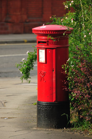 A vintage red British pillar post-box stands isolated on a London street, a symbol of old England's postal mailの写真素材