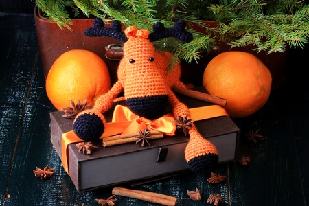 Christmas composition deer gift under the tree by hand knitted toy cinnamon, anise tangerine spruce vintage style on old wooden backgroundの写真素材