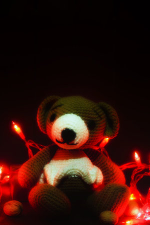 Christmas background. knitted toy bear with a burning Christmas garland on a brown backgroundの写真素材