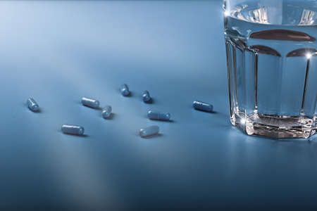 Blue pill capsules with a glass of water on a blue background. Soft selective focus.