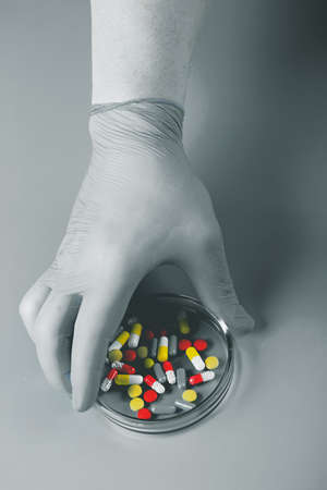 Doctor's hand holds a glass cup with multicolored pills on a gray monochrome background.の写真素材
