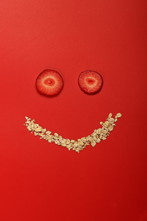 oatmeal with strawberries. Creative layout in the form of a face with a smile. Original design composition of healthy breakfast foodの写真素材