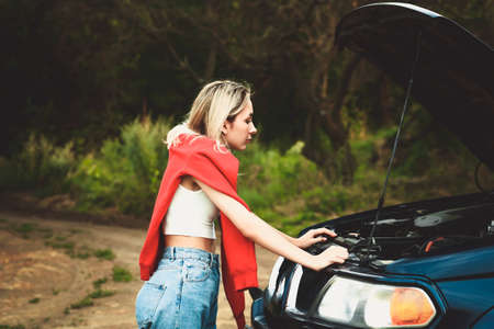 girl looks under the hood of a broken car. Soft selective focusの写真素材