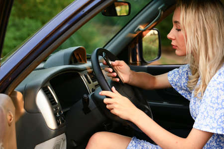 Young woman talking on a cell phone while sitting in the car in the drivers seat. Attractive blonde...