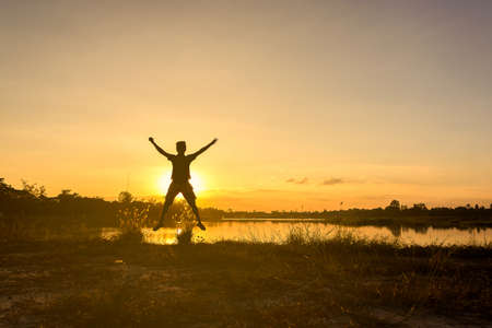 Freedom-young man is jumping at lake with sunset sky - back litの写真素材