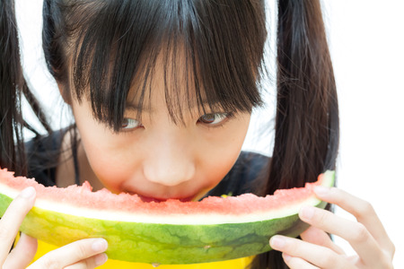 Asian girl holding and eating slice of watermelon, on white background.の写真素材