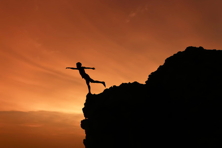 Silhouette Freedom-young man is jumping over  rocky mountains at sunset.の写真素材