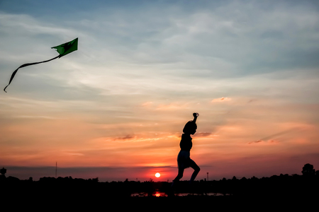Silhouette girl flying a kite in sunset background.の写真素材