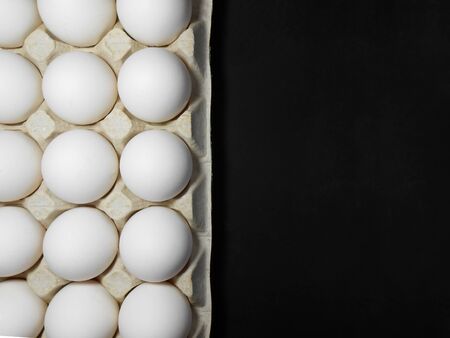 Raw chicken eggs in egg box on black background