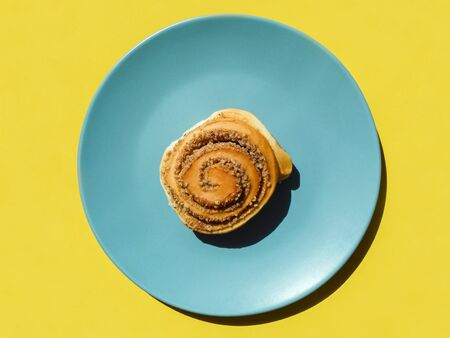 Sweet buns in blue plate isolated on yellow. Top view. Sweet cinnamon rolls pattern. hard shadowの写真素材