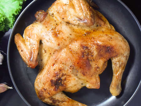 Fried roast chicken Tabaka in frying pan on black background. Top view