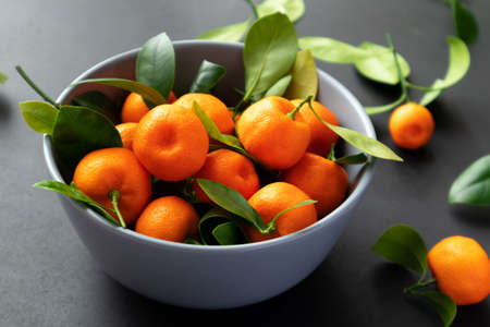 Mandarins or clementines with leaves on a black background. Tangerines in a plate.の写真素材