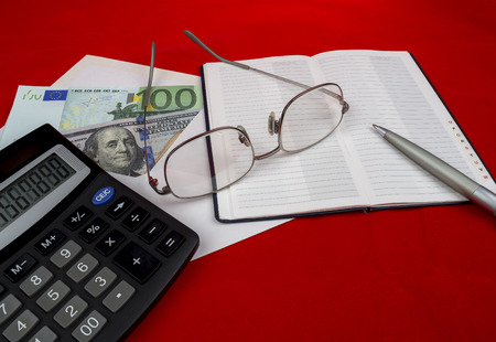 Banknotes in an envelope with a pen a notepad a calculator and glasses on a red background.の写真素材