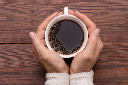 Female hands holding cups of coffee on rustic wooden table background