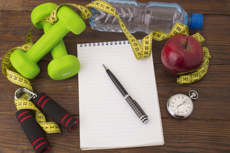 Workout and fitness dieting copy space diary. Healthy lifestyle concept. Apple, dumbbell, water, expander hand, stopwatch and measuring tape on rustic wooden table.の写真素材