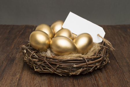 Nest with golden eggs with a tag and place for text on a wooden background. The concept of successful retirementの写真素材