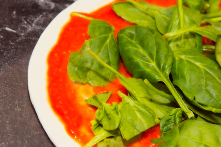 raw pizza with spinach and tomato sauceの写真素材