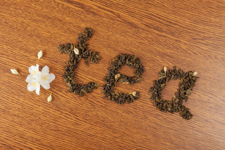 the word "tea" from leaves of green tea on a wooden surface near jasmine flowersの写真素材