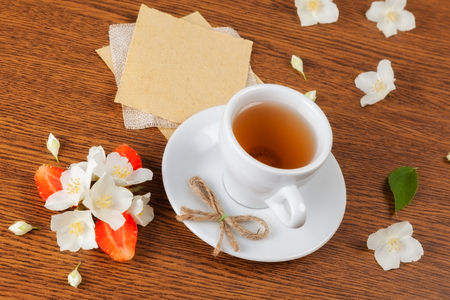 white cup of green tea. jasmine flowers with strawberry halves. texture blank for writing. still lifeの写真素材