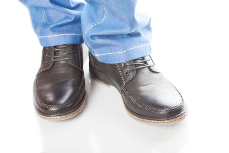 Feet in blue jeans and shoes with laces on a white background.