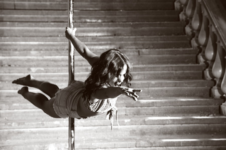 Beautiful brunette dancing on a pole on underground background.