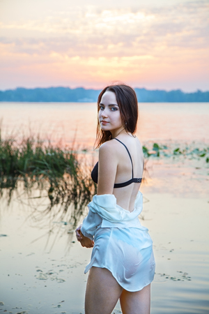an attractive girl in lingerie and a white shirt is standing by the river at dawn. beauty, fashion, portrait.の写真素材