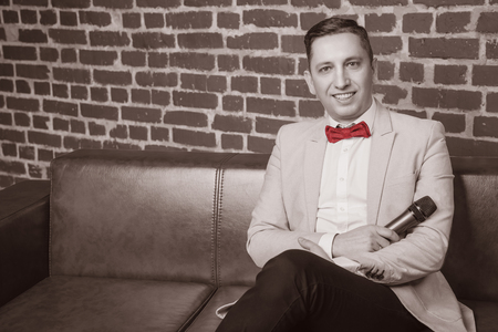 portrait of an attractive man in a suit against a brick wall with a microphoneの写真素材