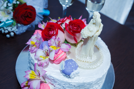 Celebratory cake with figures of the bride and groom decorated flowers and cream on table near the bride's bouquetの写真素材