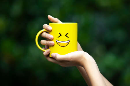 Close up of hand holding yellow glass with smiley emoticon, conceptualの写真素材