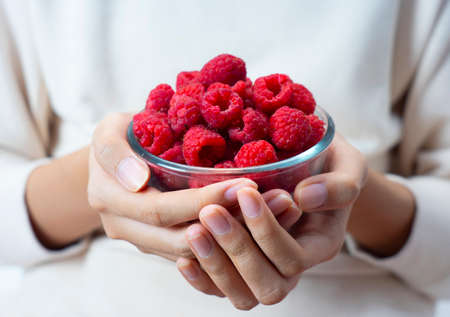 hands holding raspberries in a bowl