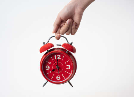 Female hand holding alarm clock on white background, copy space, conceptualの写真素材