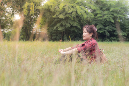 Beautiful asian woman sitting on the grass with bag and sunlight fair surrounded,Thai womanの写真素材