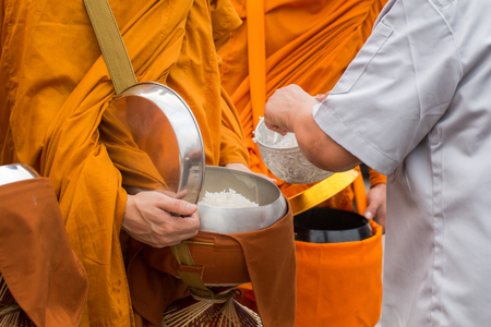 Buddhist monk of Thailand while stand in a row waiting people put rice and food offerings in their alms bowl for make meritの写真素材